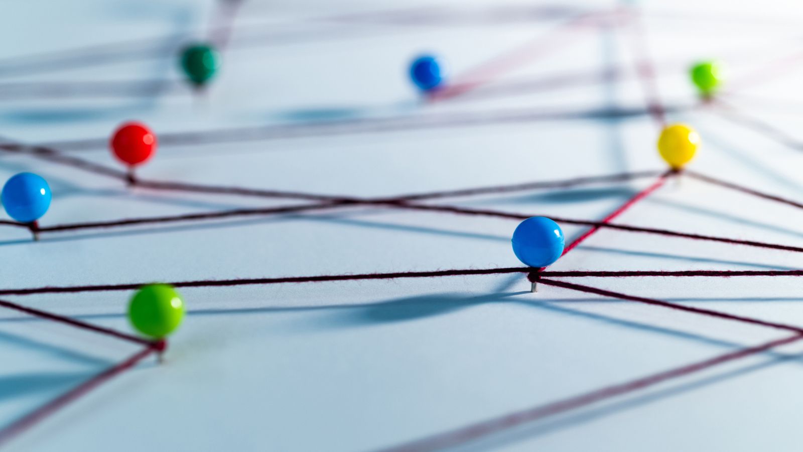 A network of colorful pins linked by strings on a board, representing how tiered AI-augmented localization components interconnect across content types