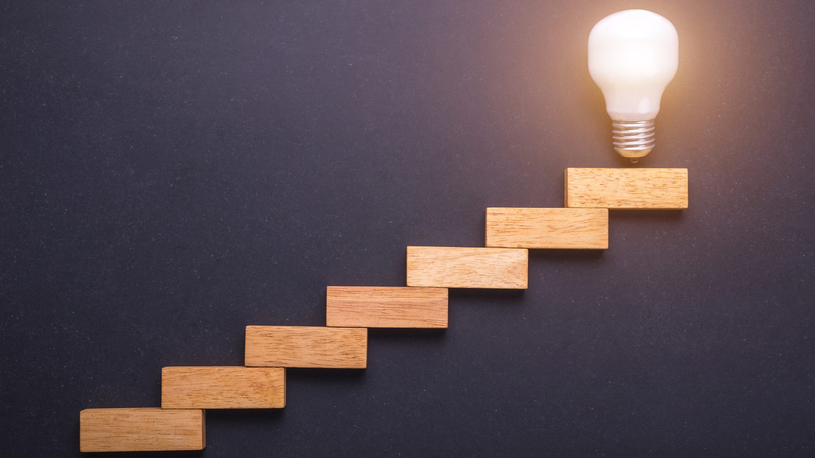 Wooden blocks rising like stairs toward a glowing light bulb showing step by step measurement of AI era localization quality